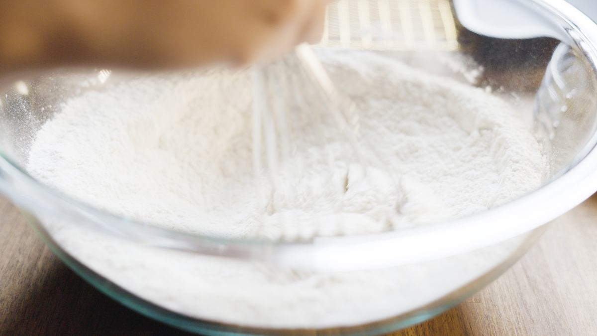 Whisk stirring sifted flour mixture in a clear glass bowl.