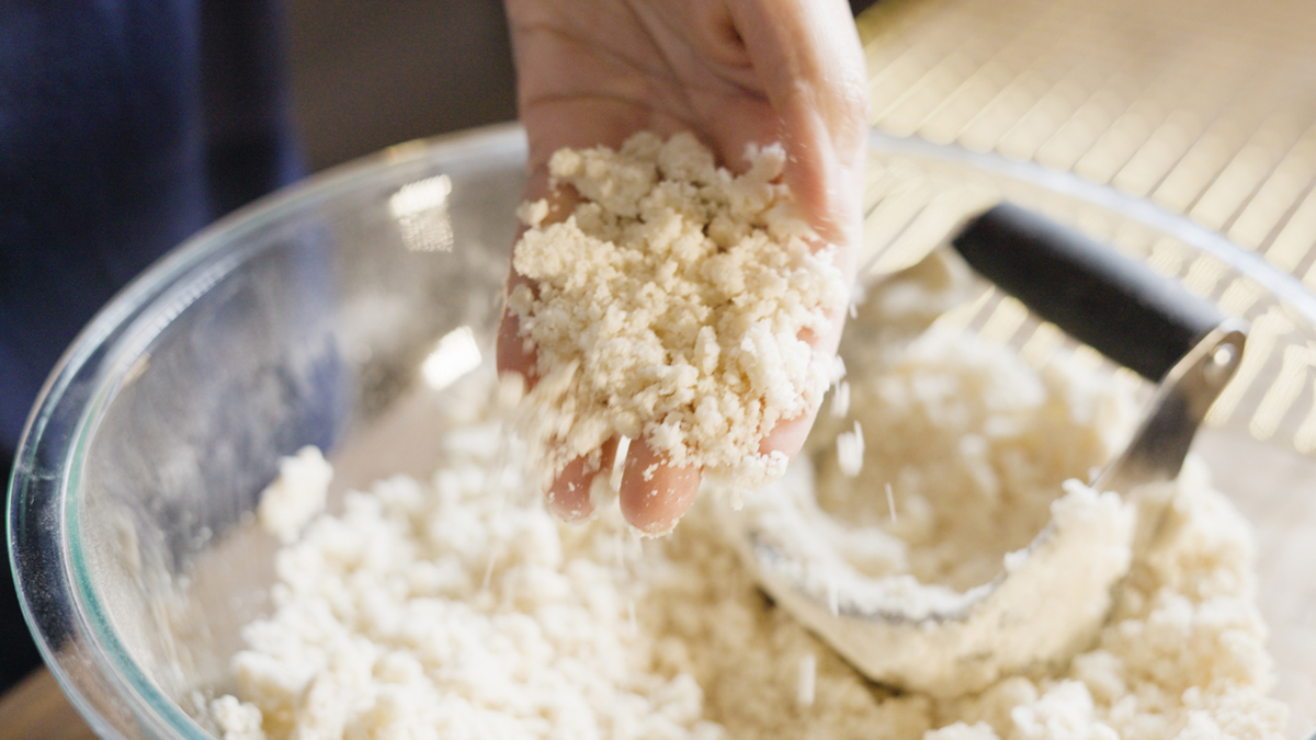 Hand holding coarse, crumbly dough after cutting shortening into the flour mixture with a pastry blender.