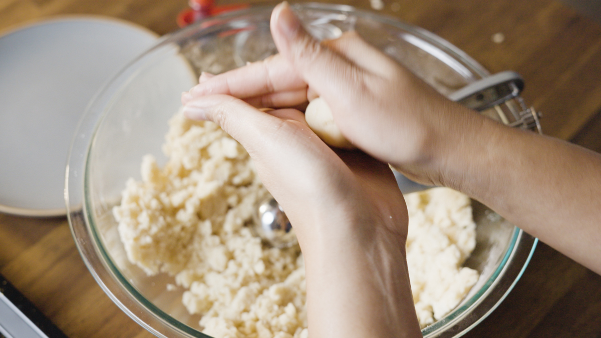 Hands pressing and rolling crumbly cookie dough into a smooth ball.