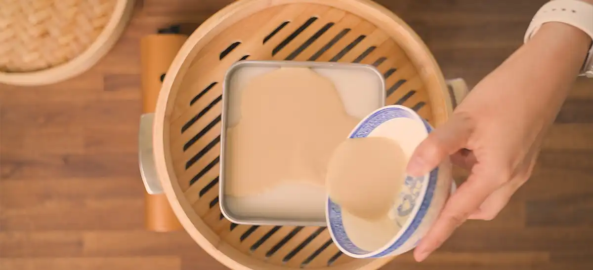 Two-panel image showing the first ladle of layered rice cake batter being poured into the square pan inside a bamboo steamer on the left, and the bamboo steamer lid being lifted to check a layer on the right
