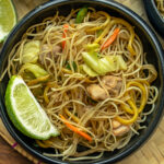 Bowl of pancit bihon with chicken, cabbage, carrots, and a lime wedge