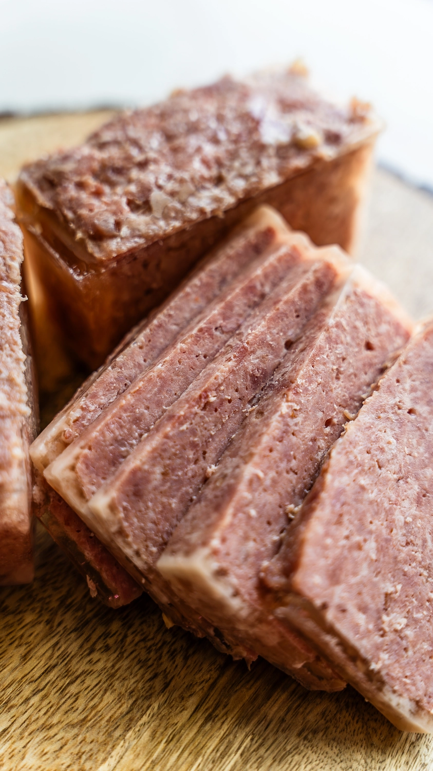 Multiple thick slices of homemade smoked SPAM fanned out on a wood cutting board showing the clean pink interior and natural marbling