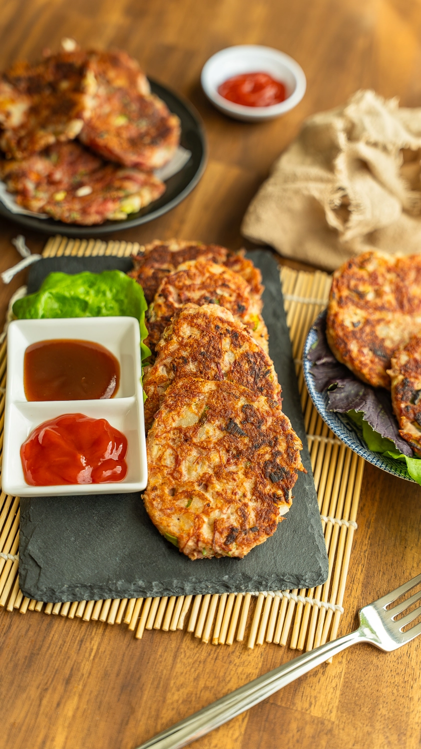 Crispy corned beef hash patties stacked on a slate board with katsu sauce and ketchup for dipping