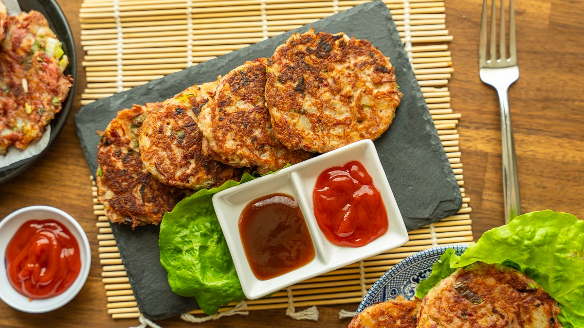 Overhead view of corned beef hash patties on a slate board with katsu sauce and ketchup for dipping