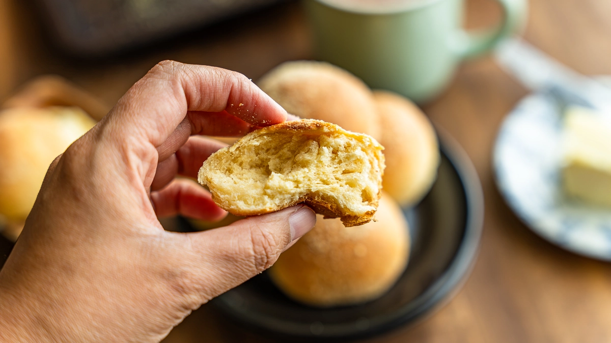 Hand holding a torn piece of pandesal, showing the soft, fluffy interior crumb.
