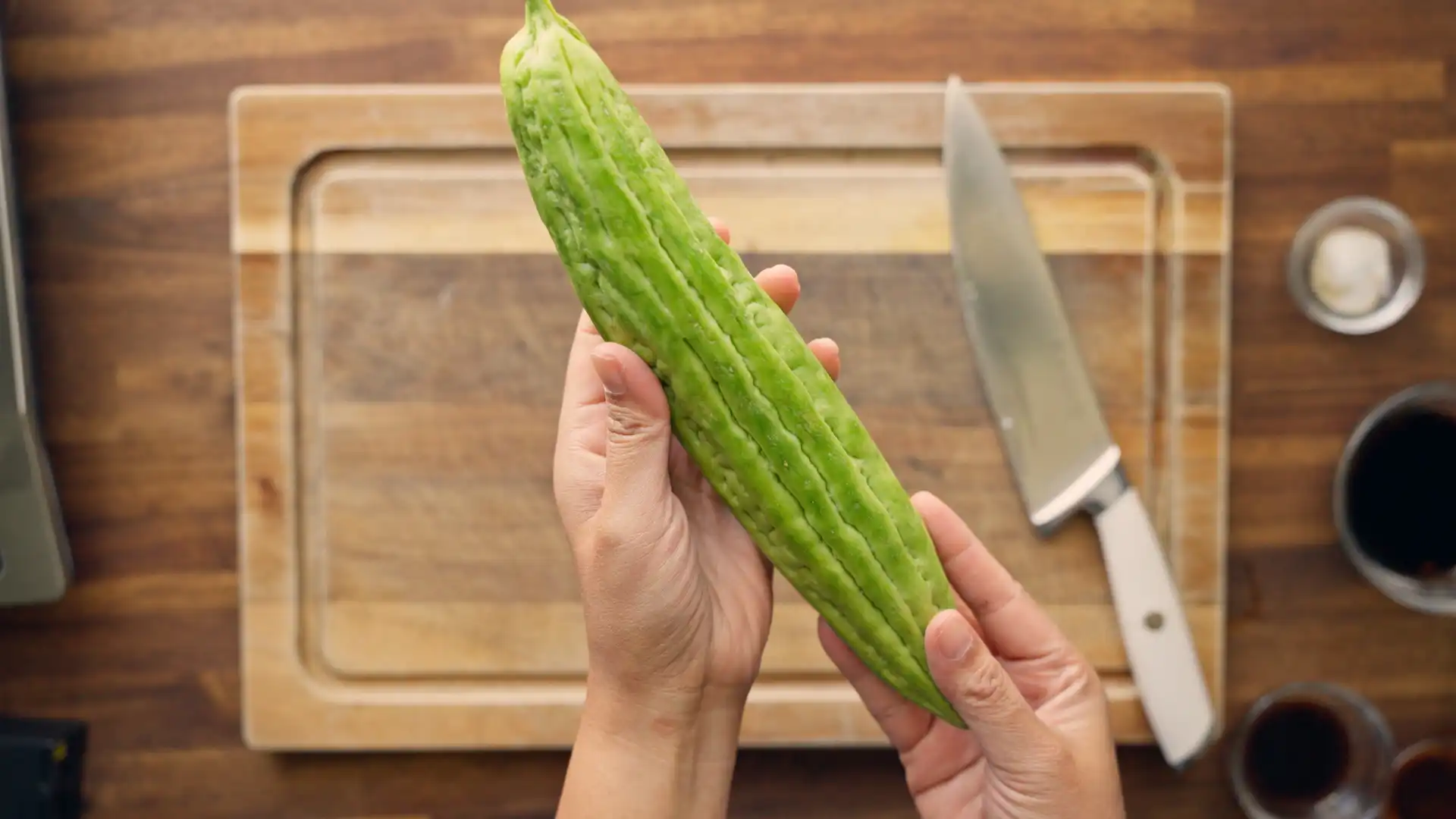 Hands holding a whole bitter melon above a cutting board before slicing
