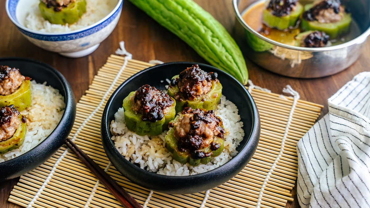 Three bowls of stuffed bitter melon with pork hash over rice, whole bitter melon in the background