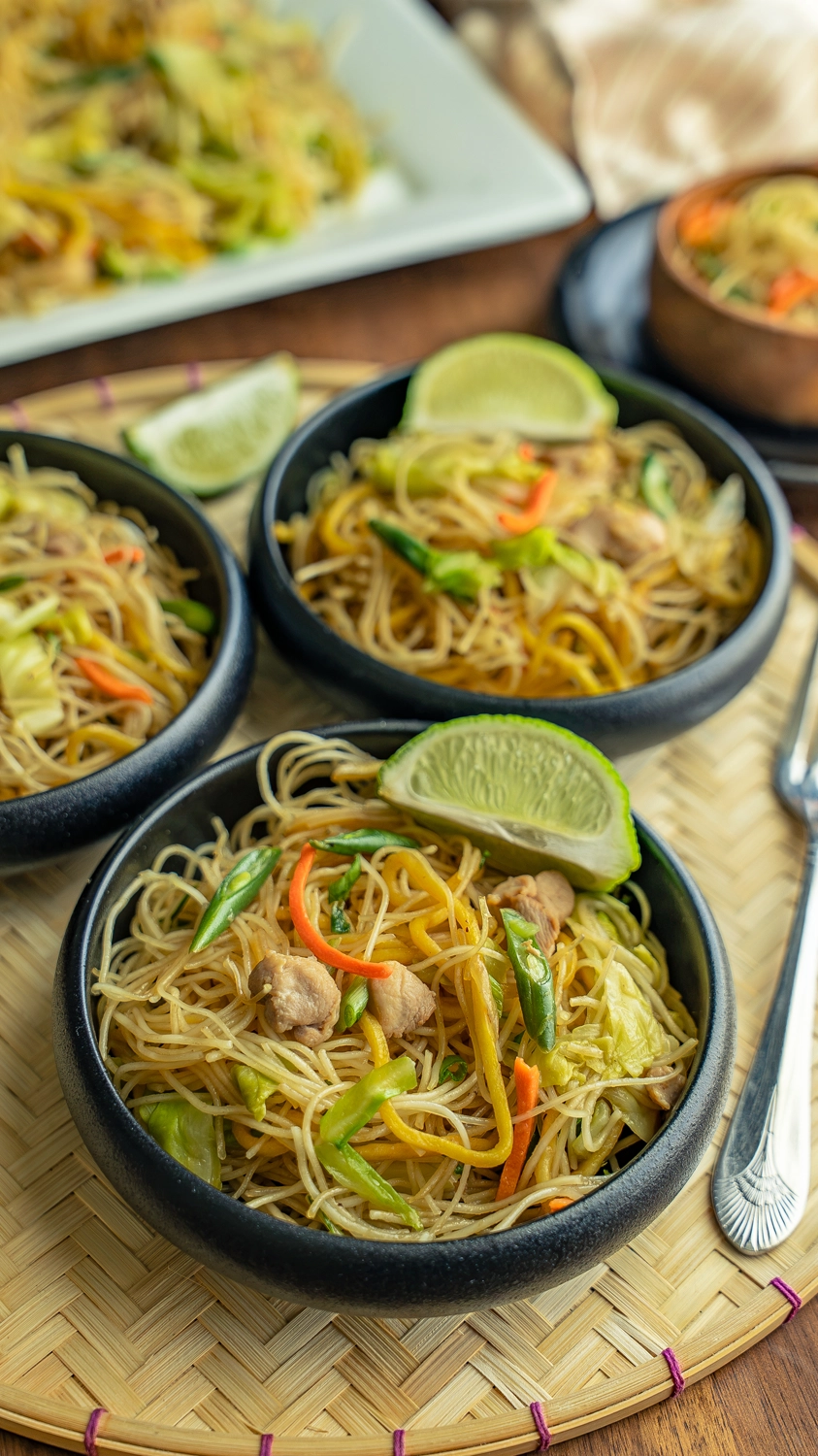 Easy pancit bihon recipe served in black bowls with lime wedges on a woven tray