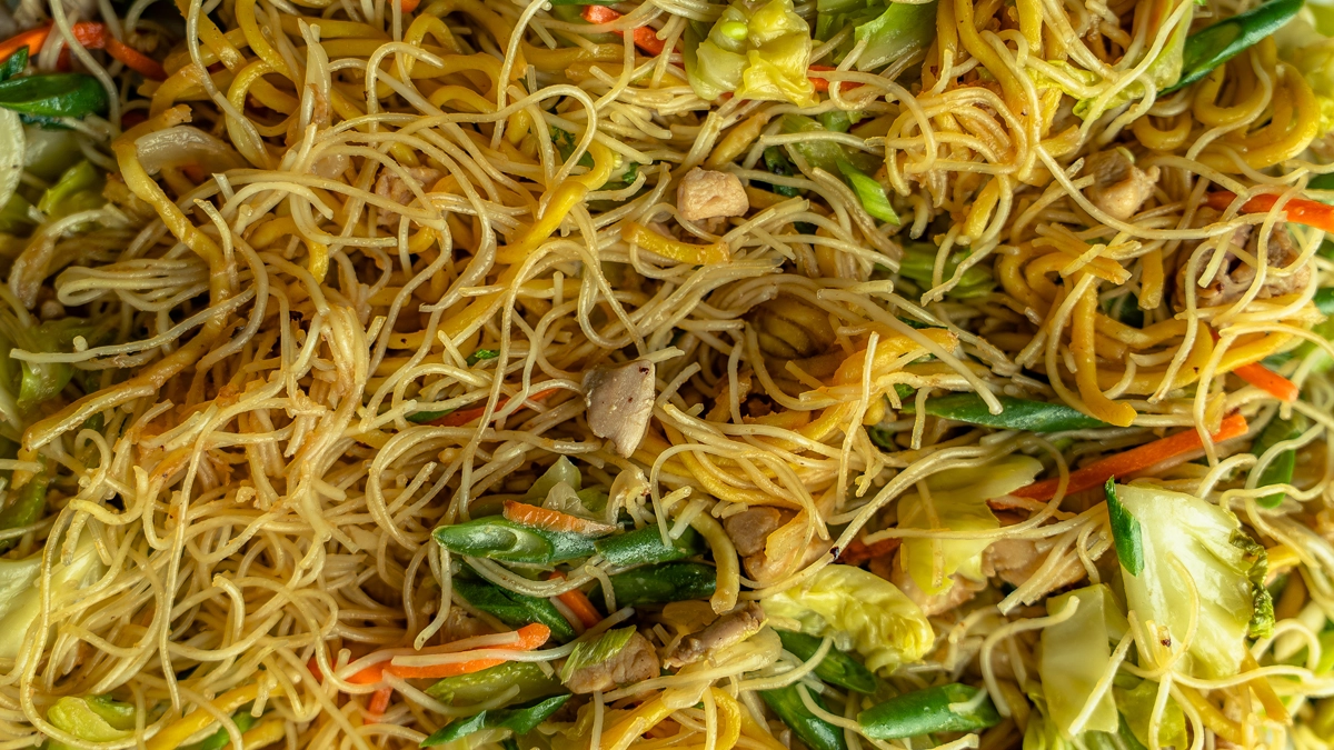 Close-up of pancit bihon noodles with chicken, cabbage, carrots, and green vegetables