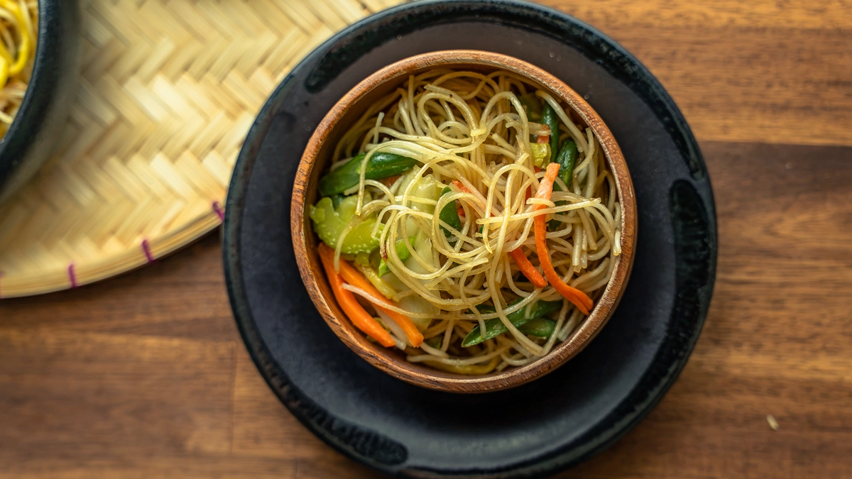 Overhead view of pancit bihon and canton noodles with carrots and green vegetables in a wooden bowl